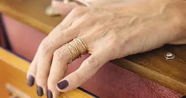 Main avec vernis fonc&eacute; et bague dor&eacute;e sur table en bois.