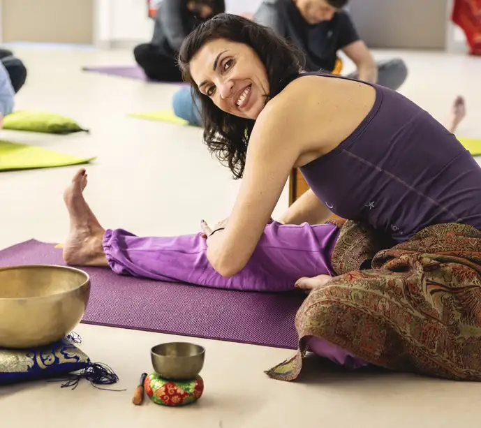 Femme souriante en yoga sur tapis violet avec bols tib&eacute;tains.