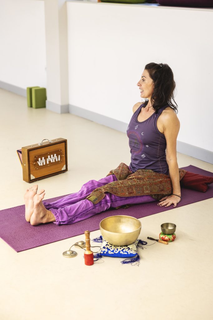 Femme assise sur un tapis de yoga avec bols chantants et harmonium.