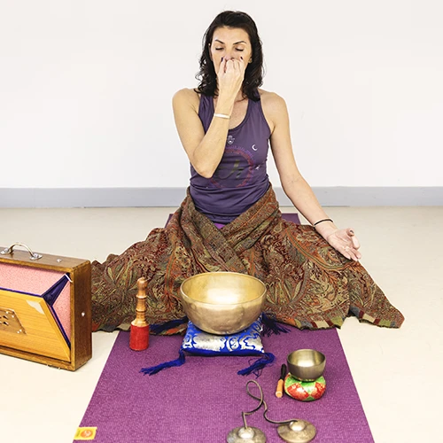 Femme méditant avec bol chantant, accessoires de yoga autour.