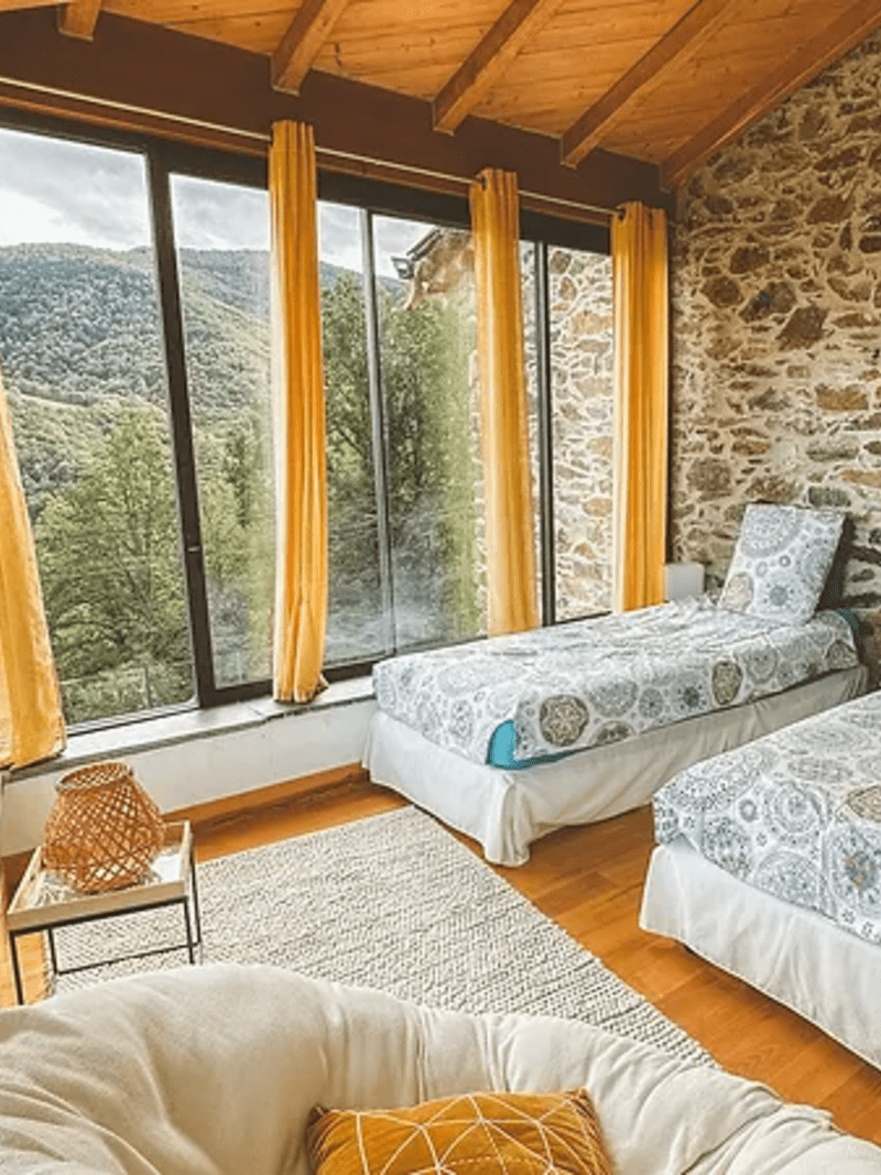 Chambre lumineuse avec lits jumeaux, grandes fenêtres et vue sur la nature.