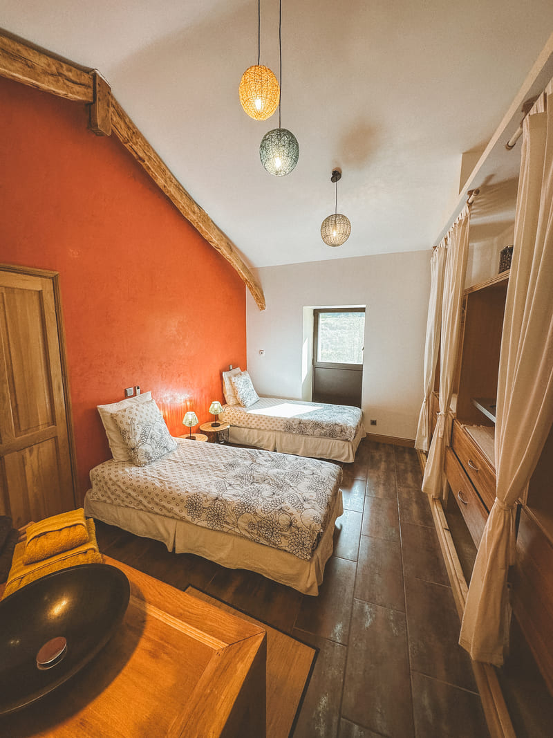 Deux lits simples dans une chambre avec mur orange et lampes suspendues.