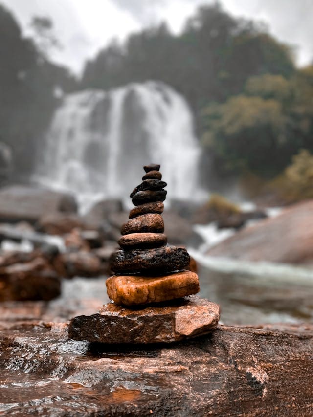 Cairn de pierres empil&eacute;es devant une cascade en arri&egrave;re-plan.