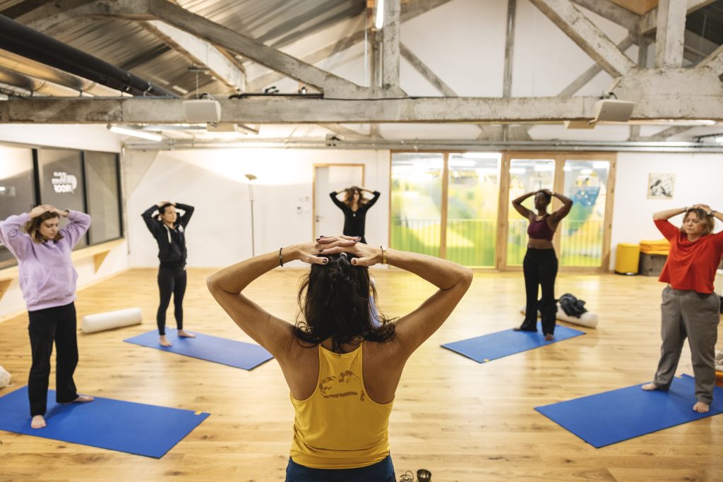 Groupe de personnes faisant du yoga sur des tapis bleus dans une salle lumineuse.