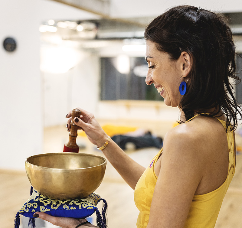 Femme souriante jouant un bol tib&eacute;tain dans un studio de yoga.