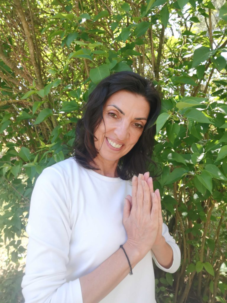 Femme en pri&egrave;re souriante devant des buissons verts.