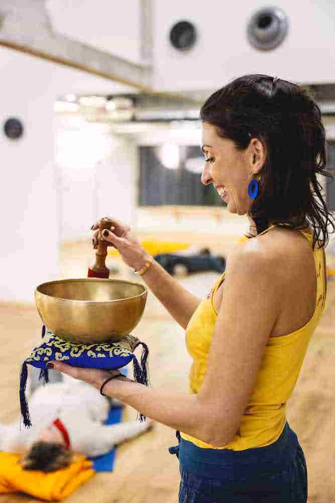 Femme souriante jouant d'un bol tibétain dans une salle de méditation.