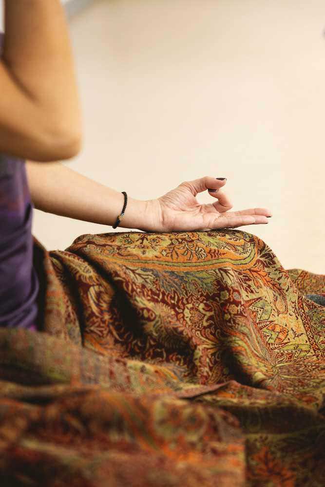 Main en position de méditation sur une couverture ornée de motifs colorés.