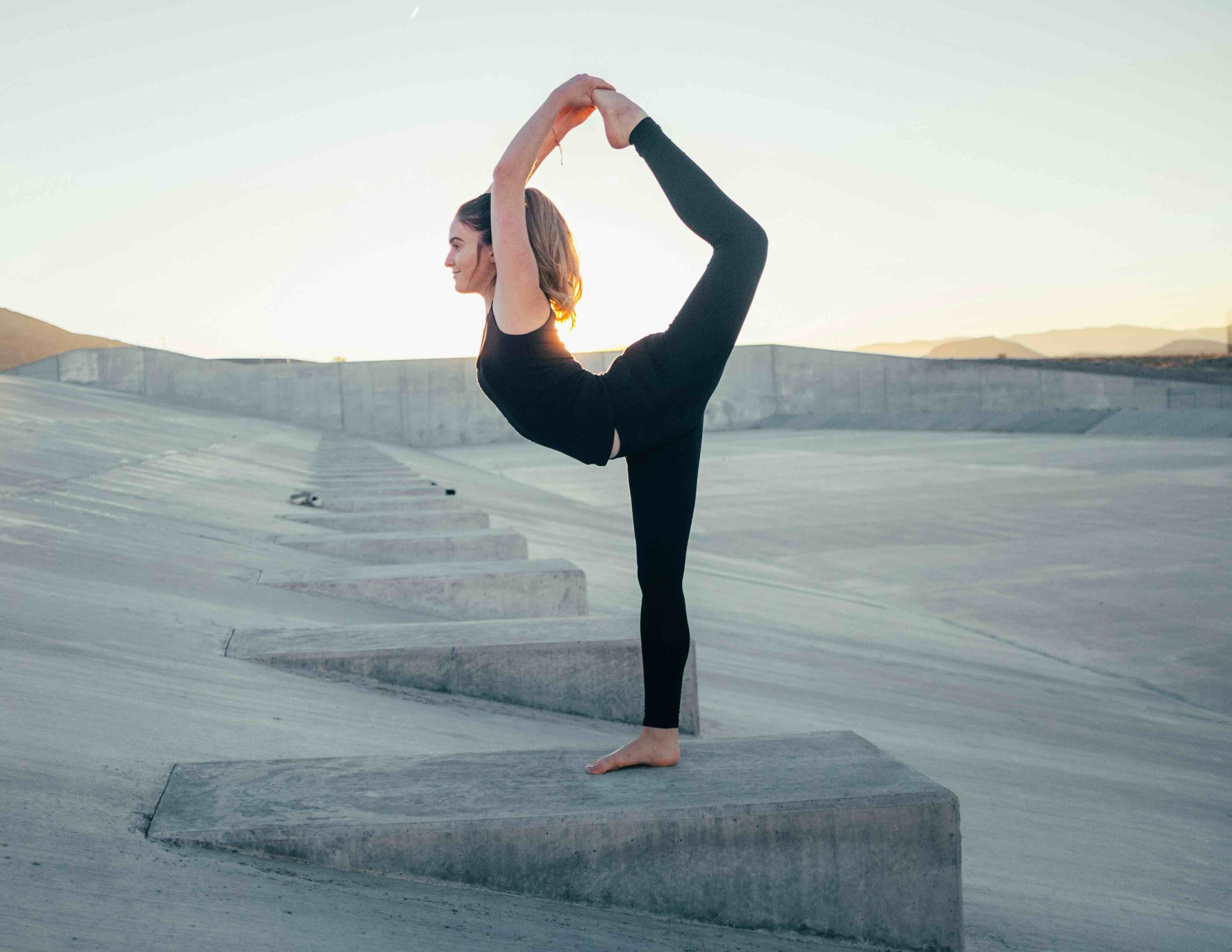 Femme faisant du yoga sur structure en béton au coucher du soleil.