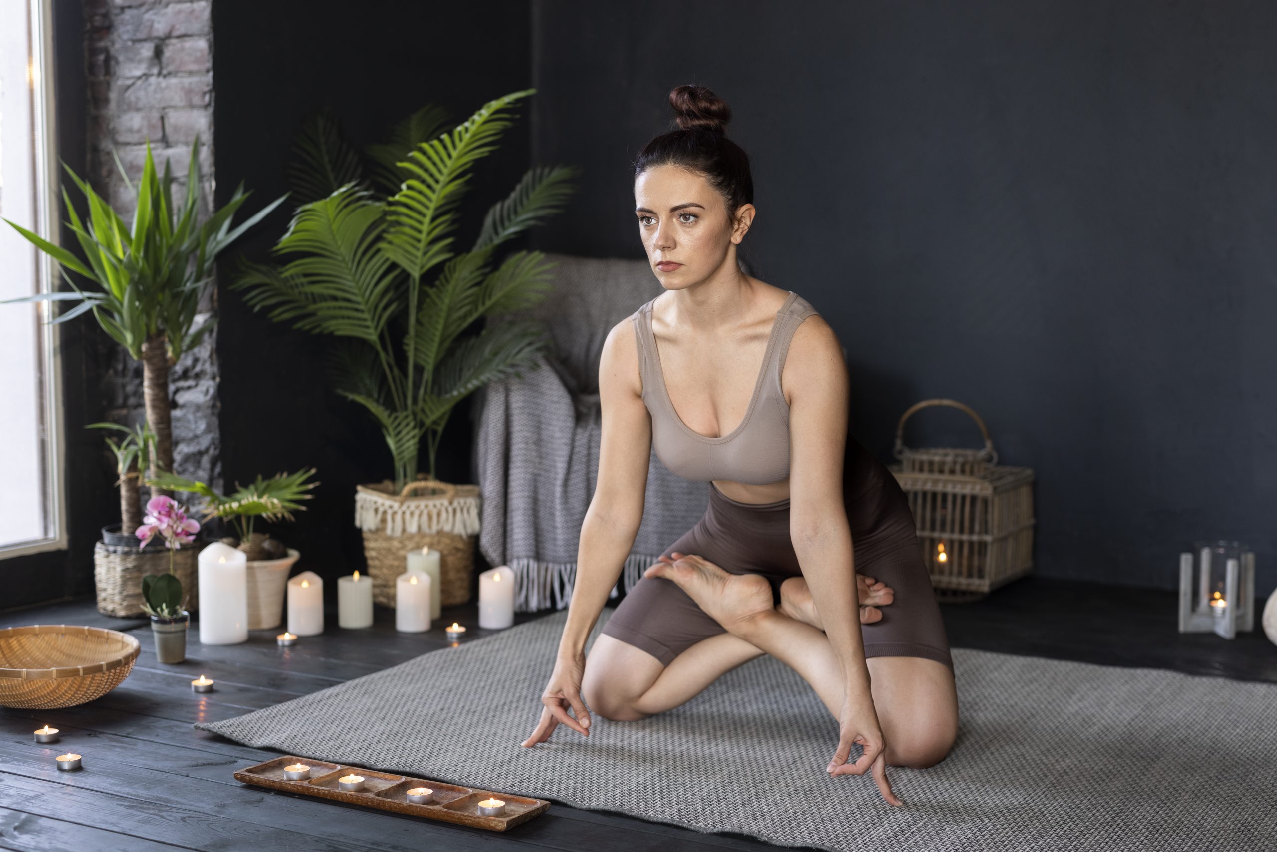 Femme en posture de yoga entourée de plantes et bougies sur un tapis.