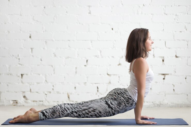 Femme en posture de yoga Urdhva Mukha Svanasana sur tapis, mur blanc en arri&egrave;re-plan.