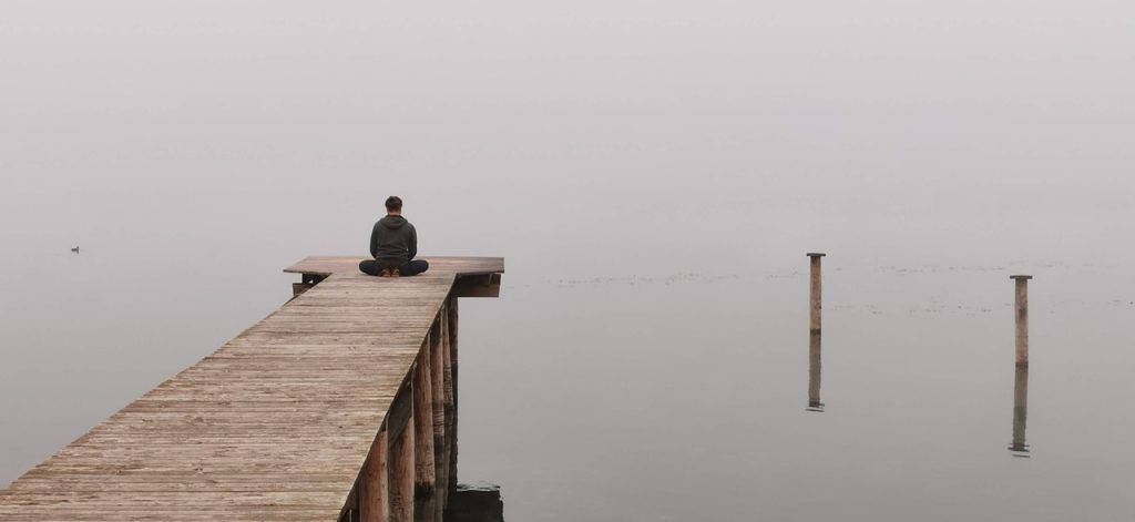 Personne méditant au bout d'un ponton sur un lac brumeux.