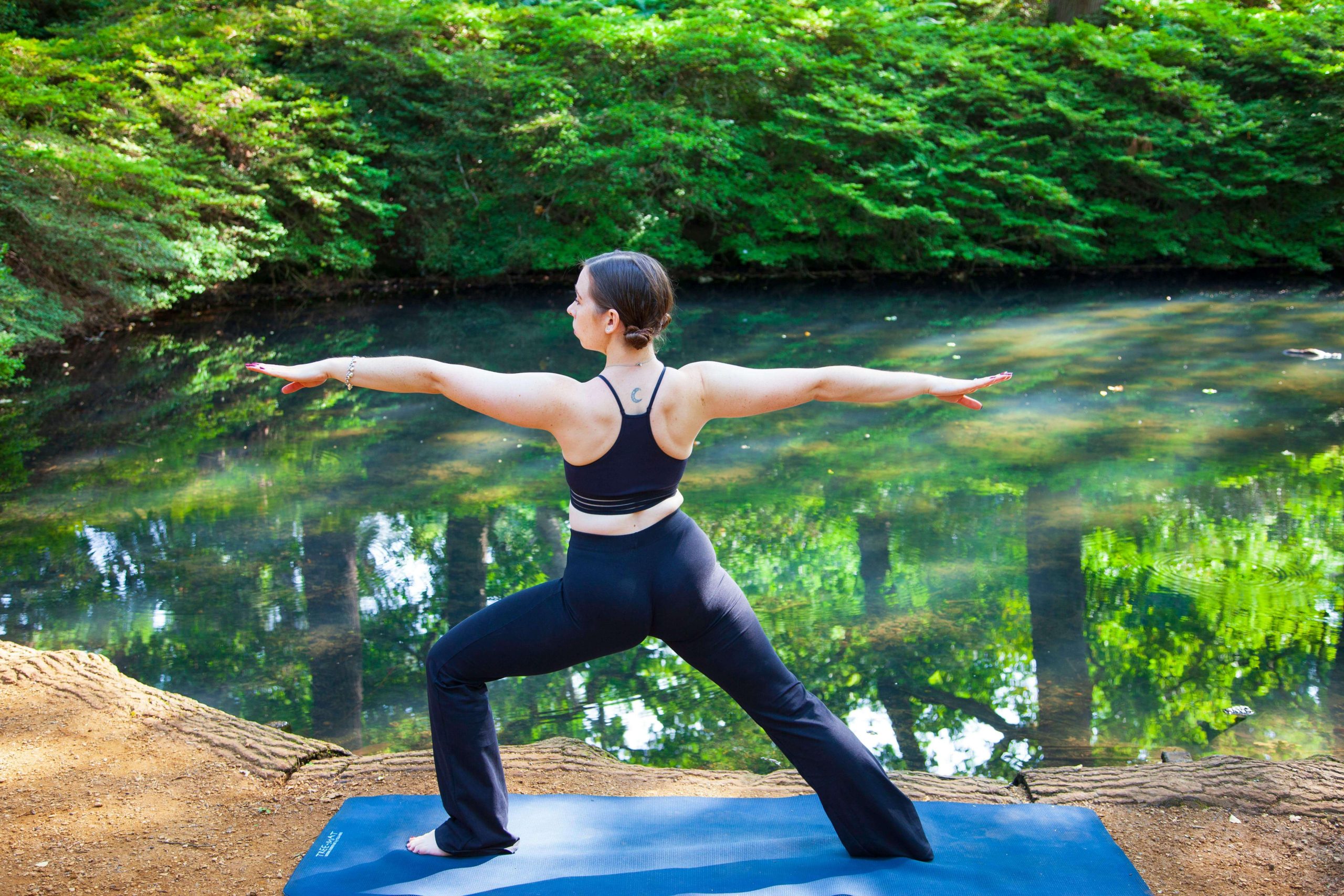 Femme en posture de yoga près d'un étang dans la nature.