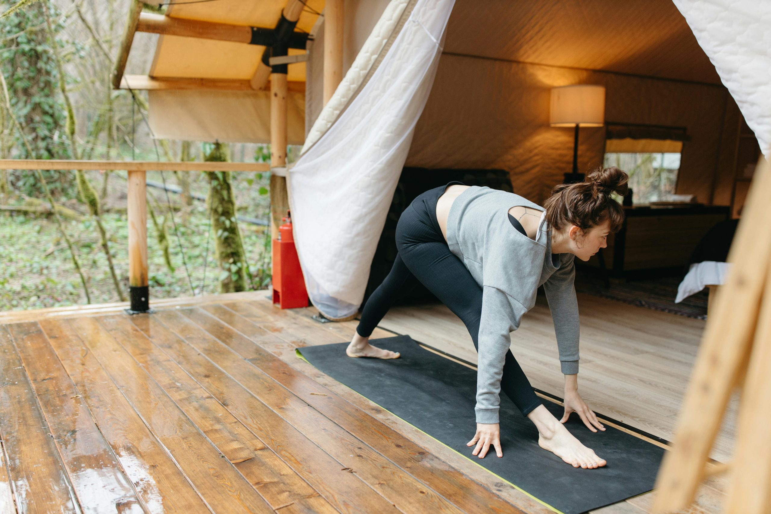 Femme pratiquant le yoga sur un tapis dans une tente en bois.