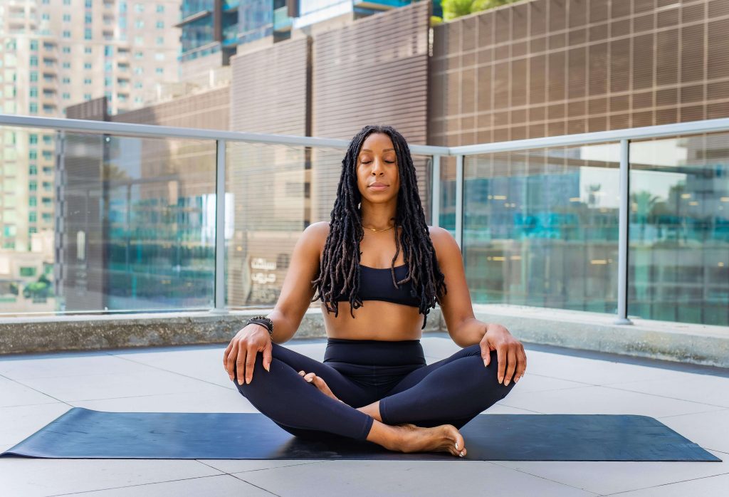 Femme méditant en position du lotus sur un tapis de yoga en extérieur.