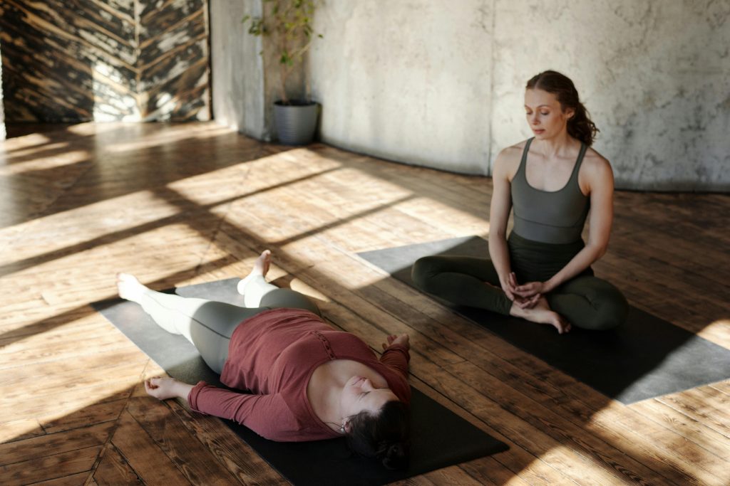Deux femmes pratiquant le yoga dans une salle ensoleill&eacute;e.