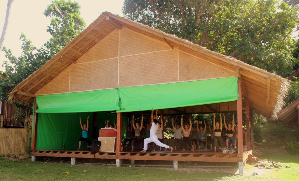Groupe faisant du yoga dans un pavillon ouvert entouré de verdure.