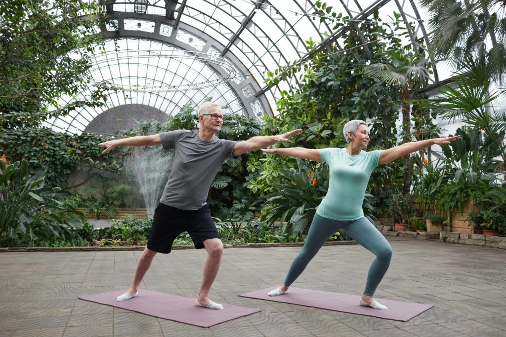 Couple senior faisant du yoga dans une serre verdoyante.