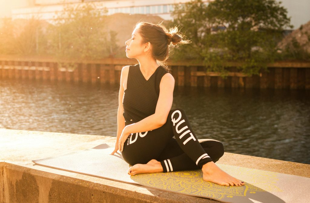 Femme faisant du yoga au bord de l'eau, éclairée par le soleil couchant.