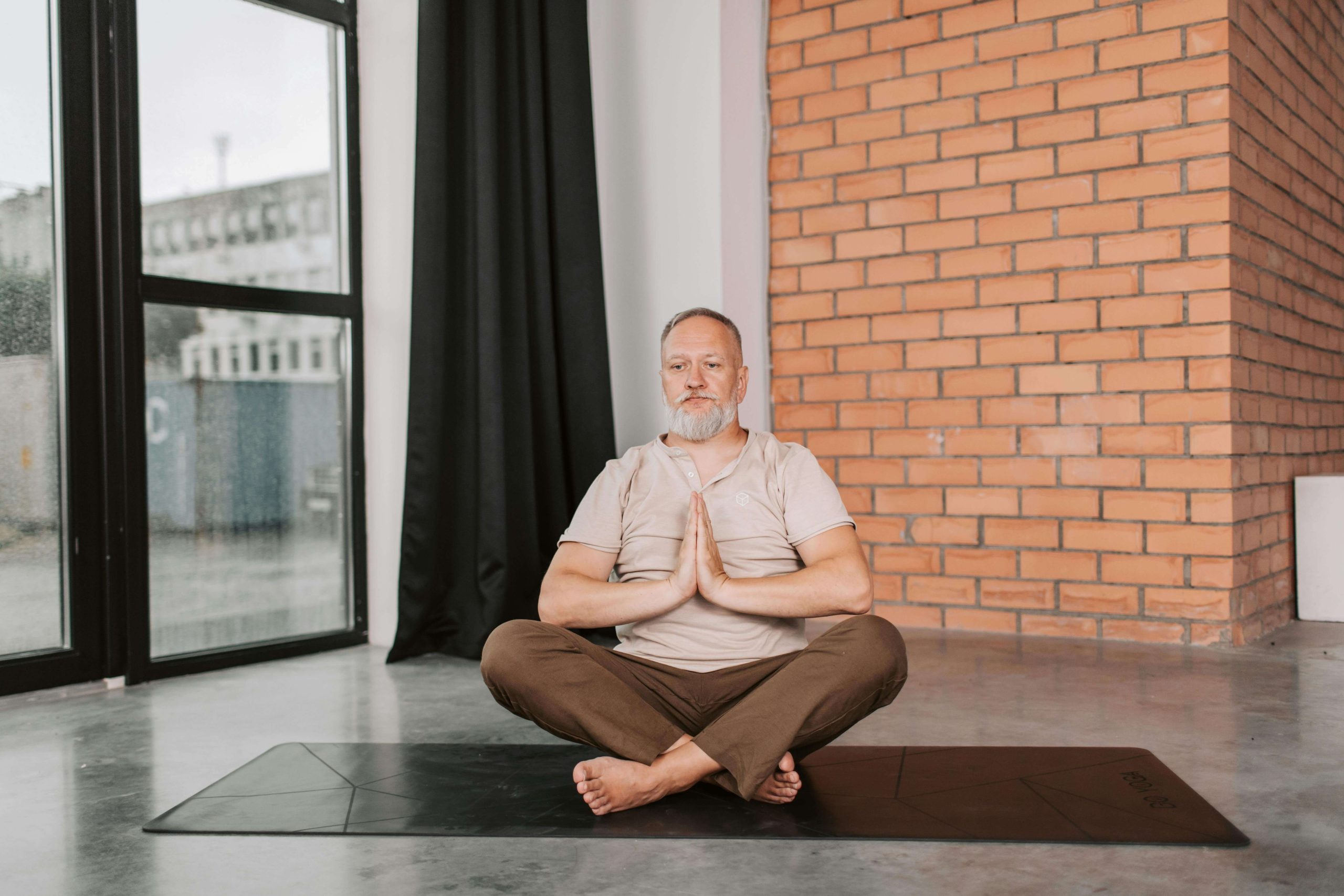 Homme méditant en position de yoga sur un tapis, mur en briques.