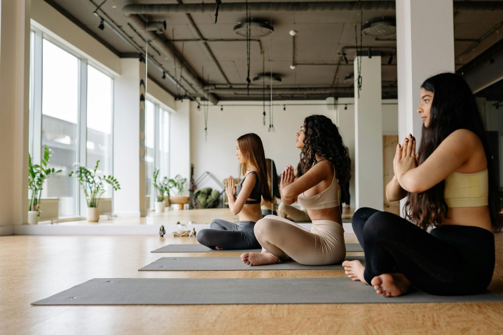 Trois femmes m&eacute;ditant en position de yoga dans une salle lumineuse.