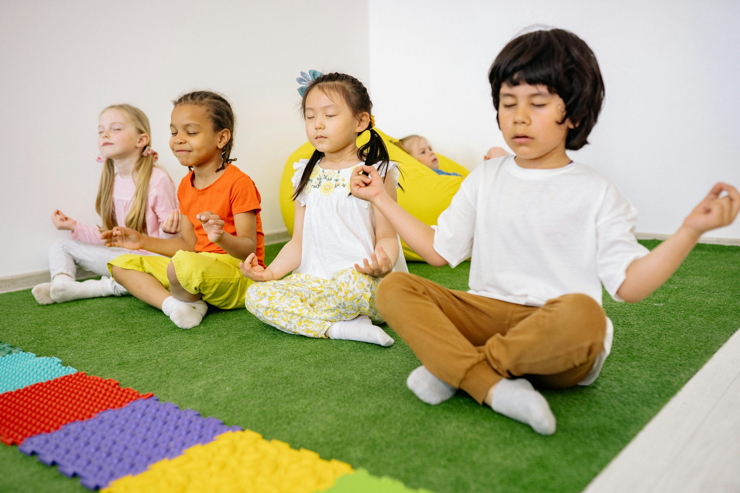 Enfants méditant assis sur un tapis vert.