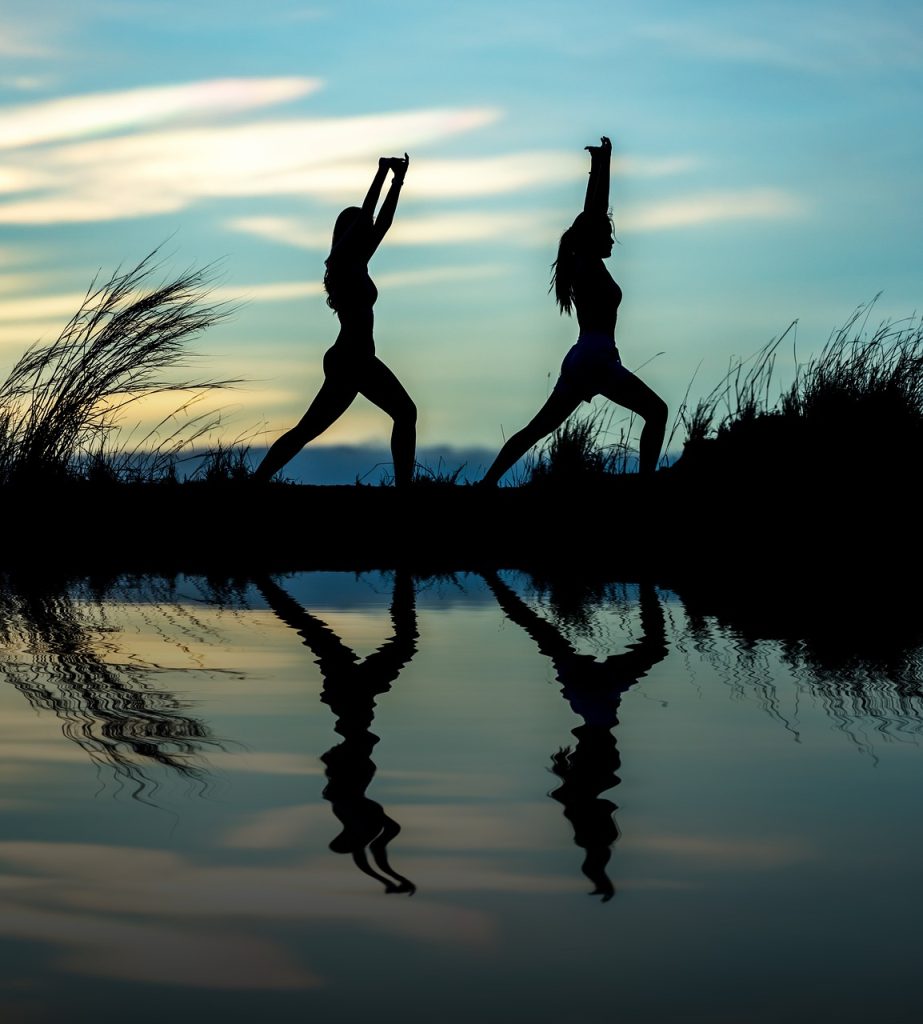Deux femmes font du yoga au bord de l'eau au coucher du soleil.