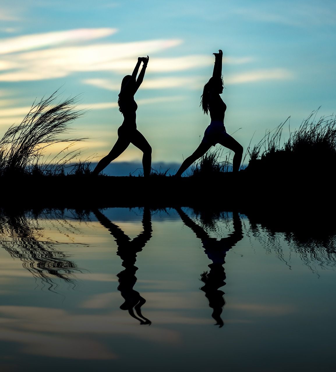 Deux femmes font du yoga au bord de l'eau au coucher du soleil.