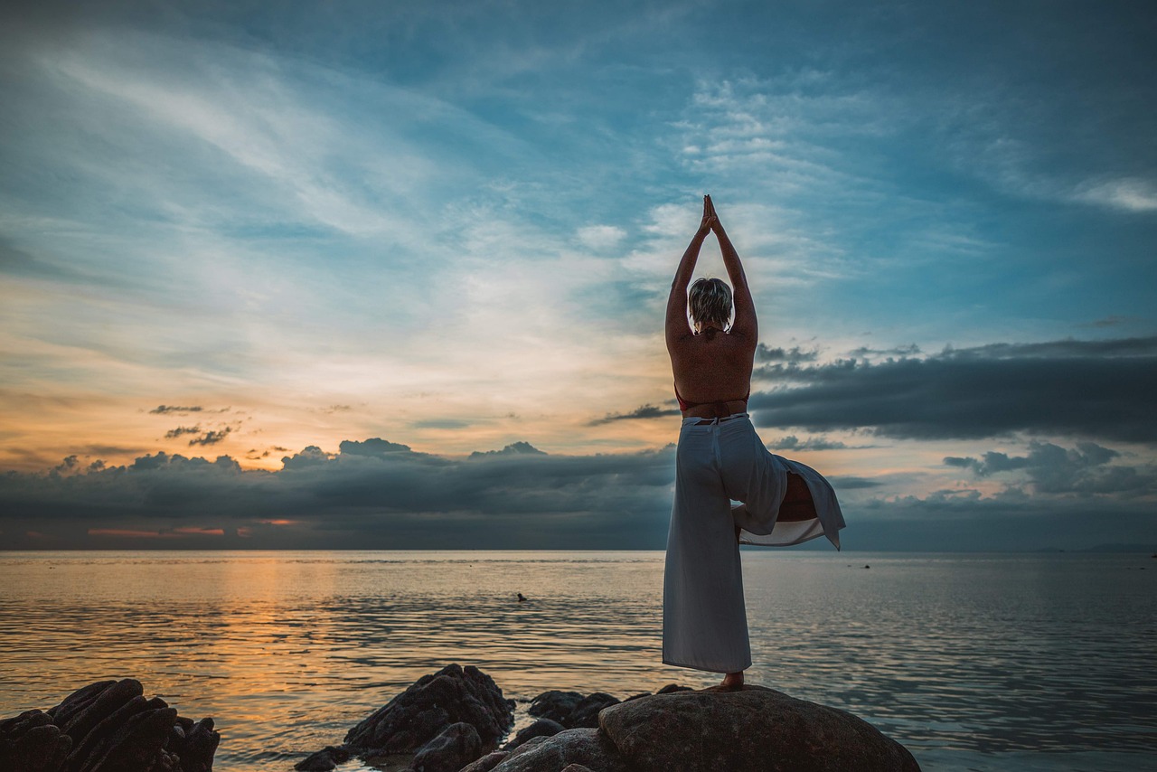 Personne faisant du yoga sur des rochers au bord de la mer au coucher du soleil.