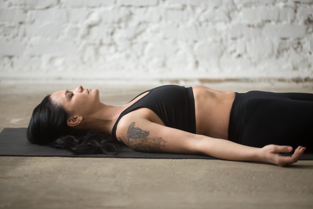Femme allongée en savasana sur un tapis de yoga dans un loft.