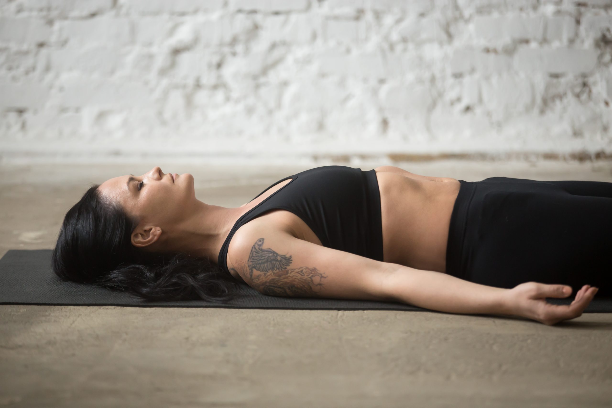 Femme allongée en savasana sur un tapis de yoga dans un loft.