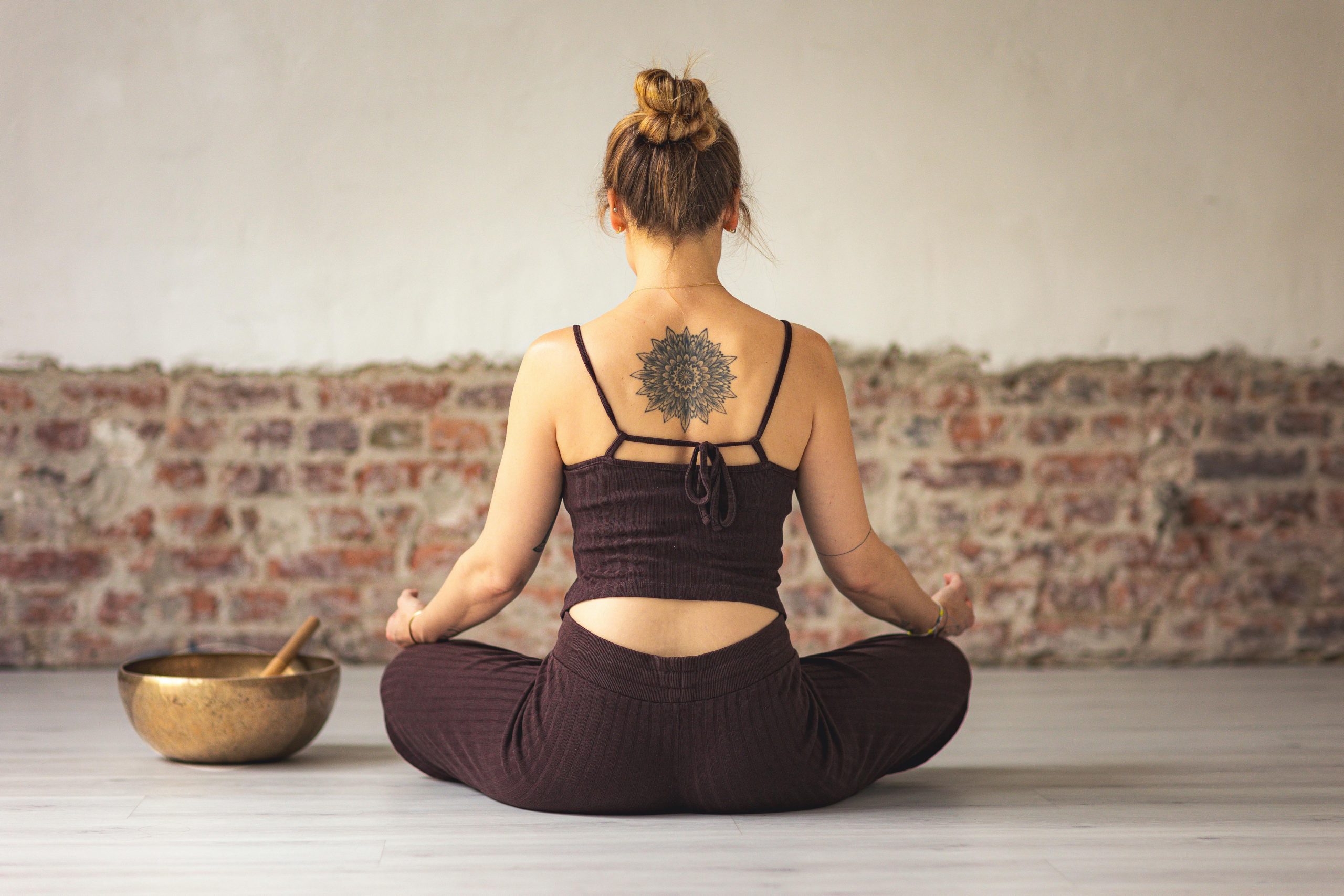 Femme méditant en position du lotus avec un tatouage dans le dos.