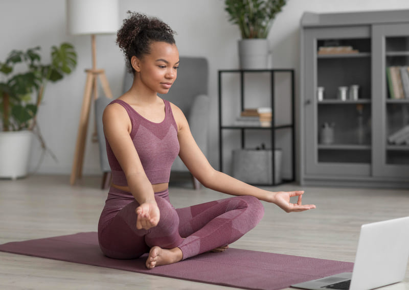Femme en position de yoga m&eacute;ditant devant un ordinateur portable.
