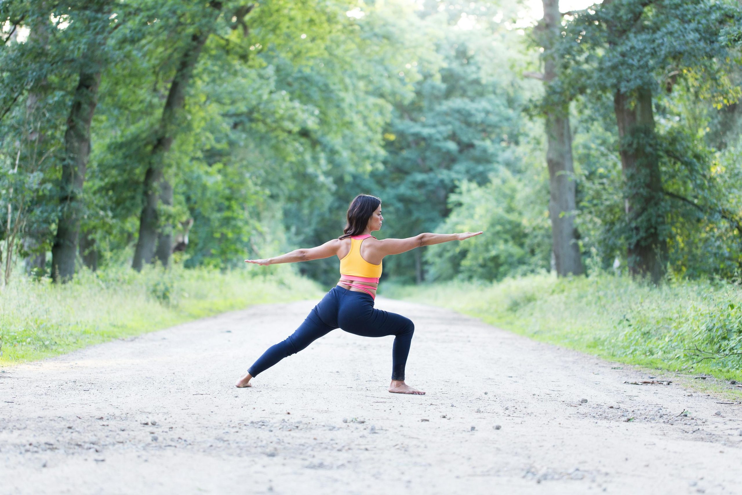 Femme faisant du yoga sur un chemin forestier.