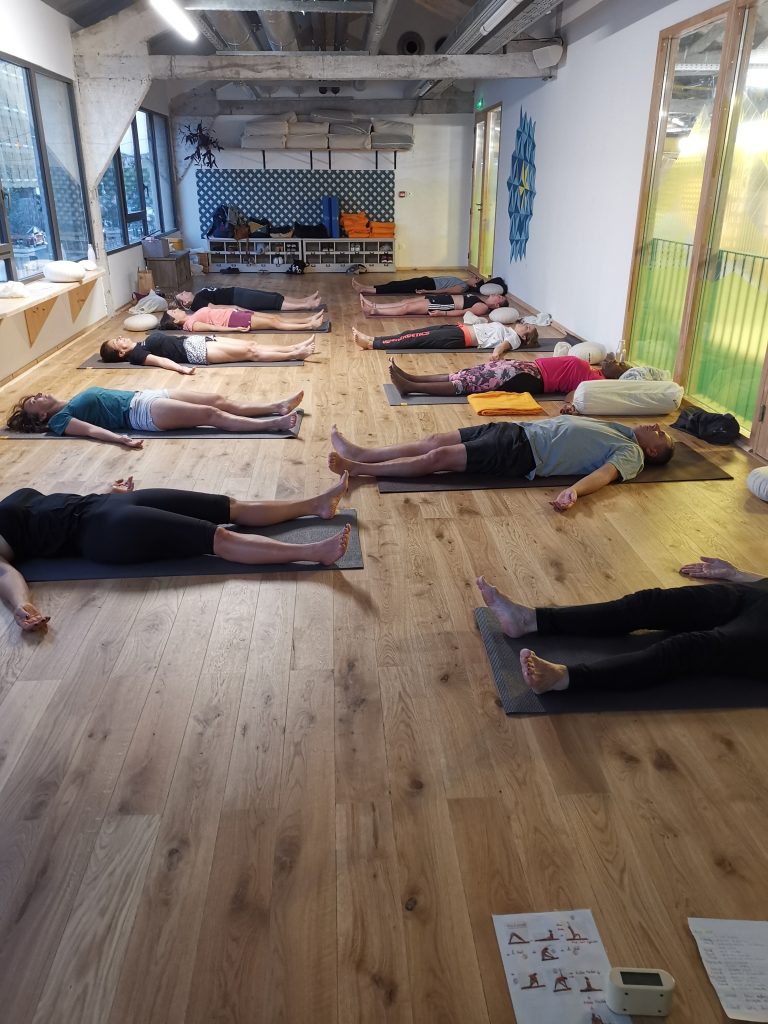 Personnes en relaxation sur des tapis dans une salle de yoga lumineuse.