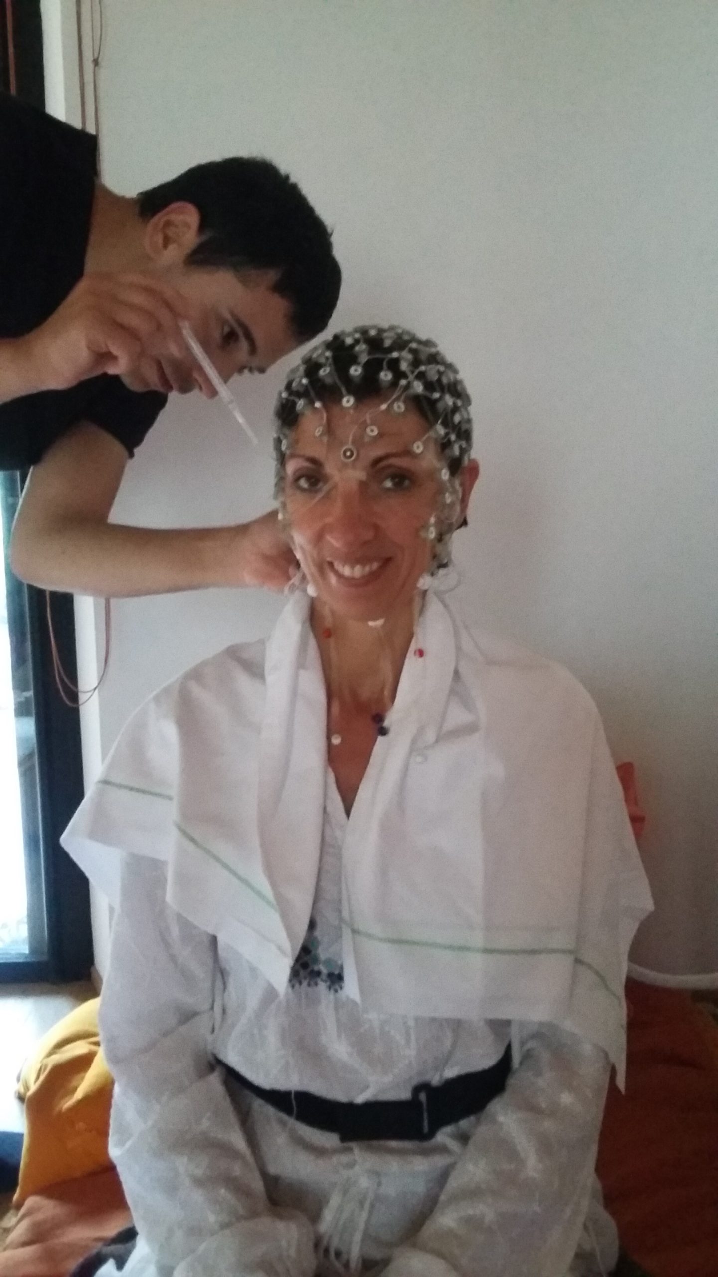 Personne souriante portant un bonnet d'électrodes, assistée par un technicien.