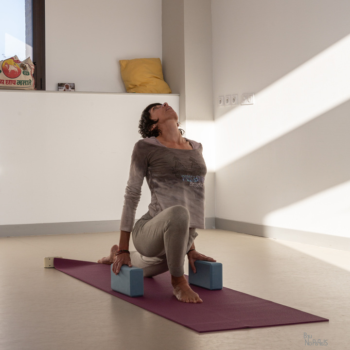 Femme faisant une posture de yoga sur un tapis avec des blocs bleus.