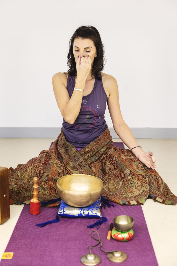 Femme m&eacute;ditant avec des bols chantants tib&eacute;tains sur un tapis violet.