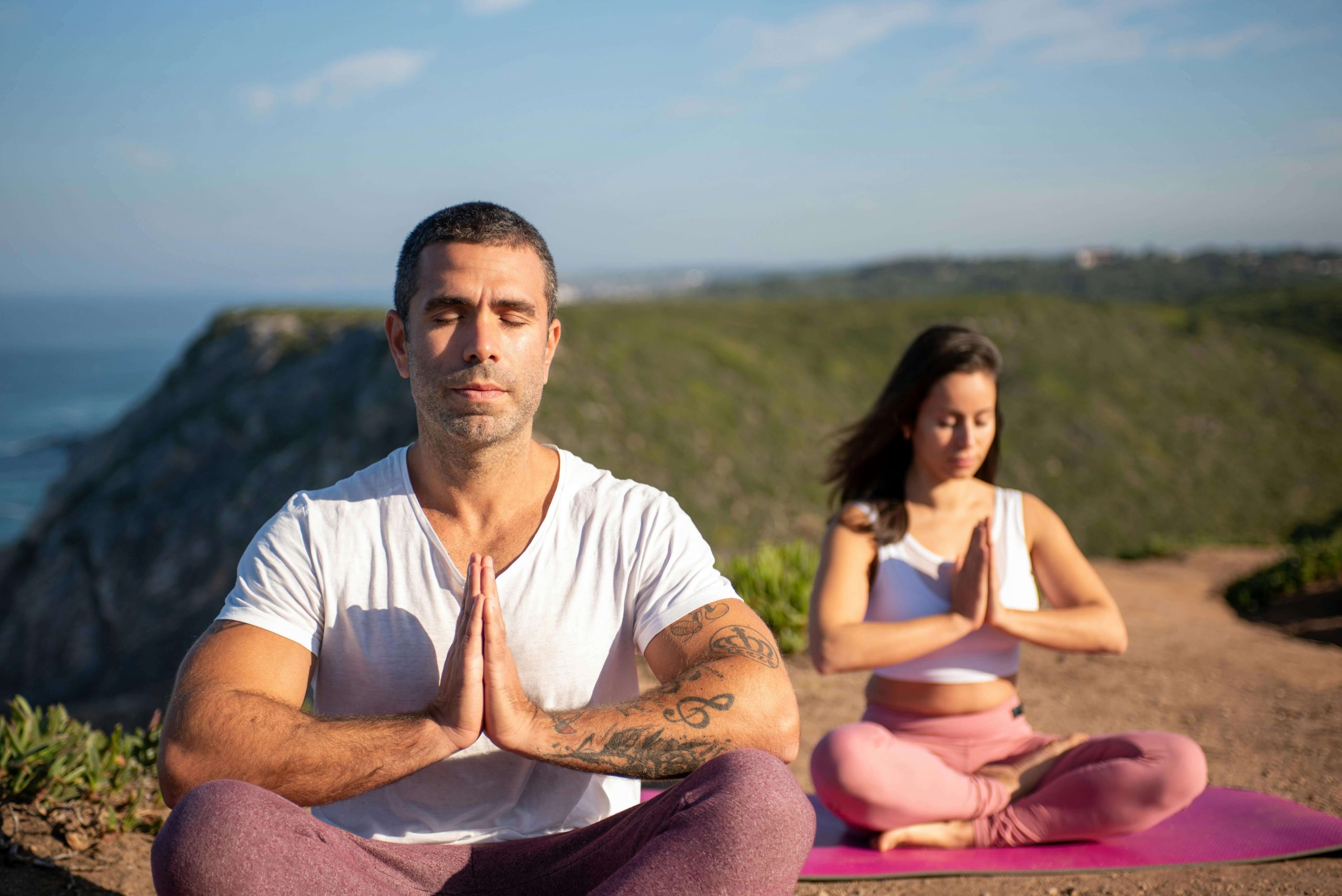 Deux personnes méditent en plein air, assises en position de yoga.