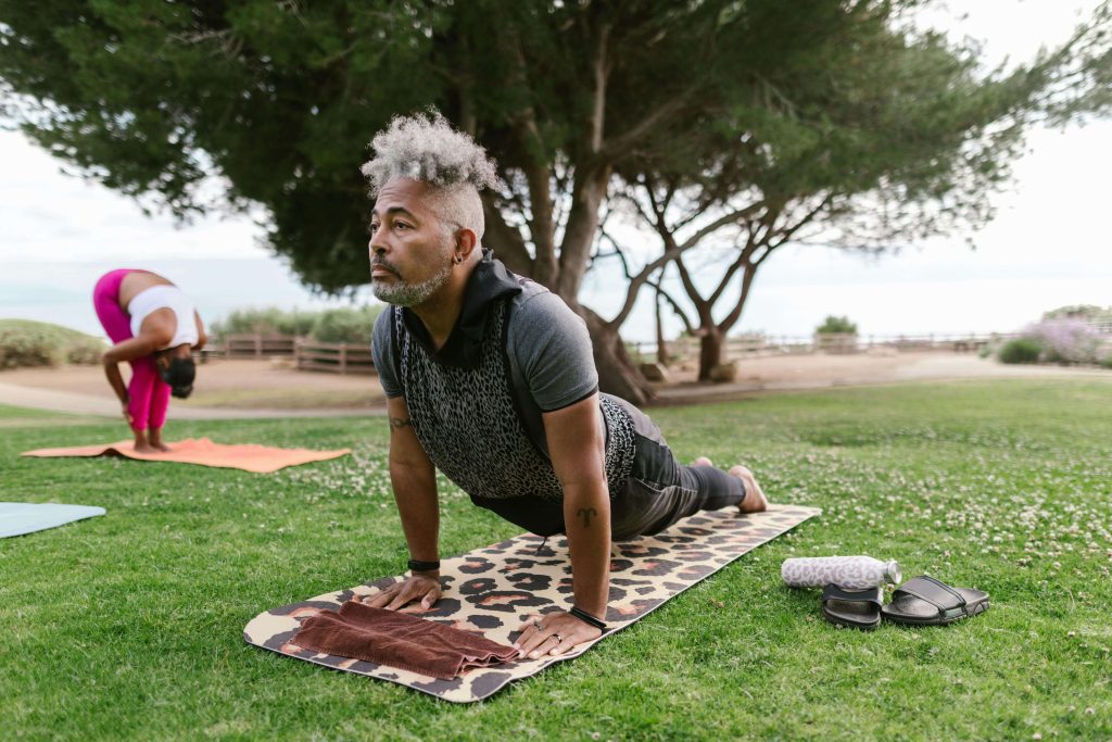 Homme et femme faisant du yoga sur des tapis en extérieur.
