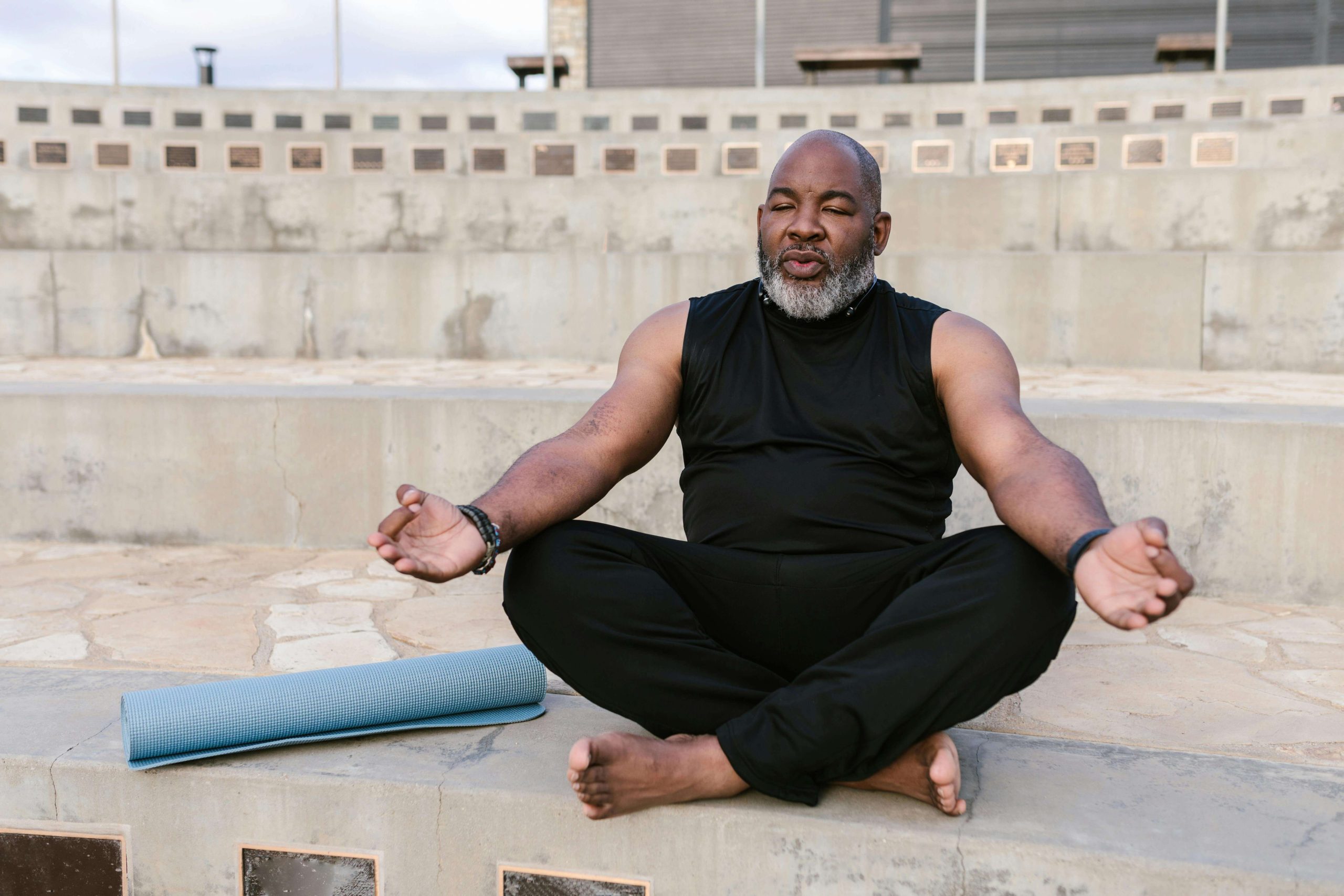 Homme méditant en extérieur avec un tapis de yoga bleu.