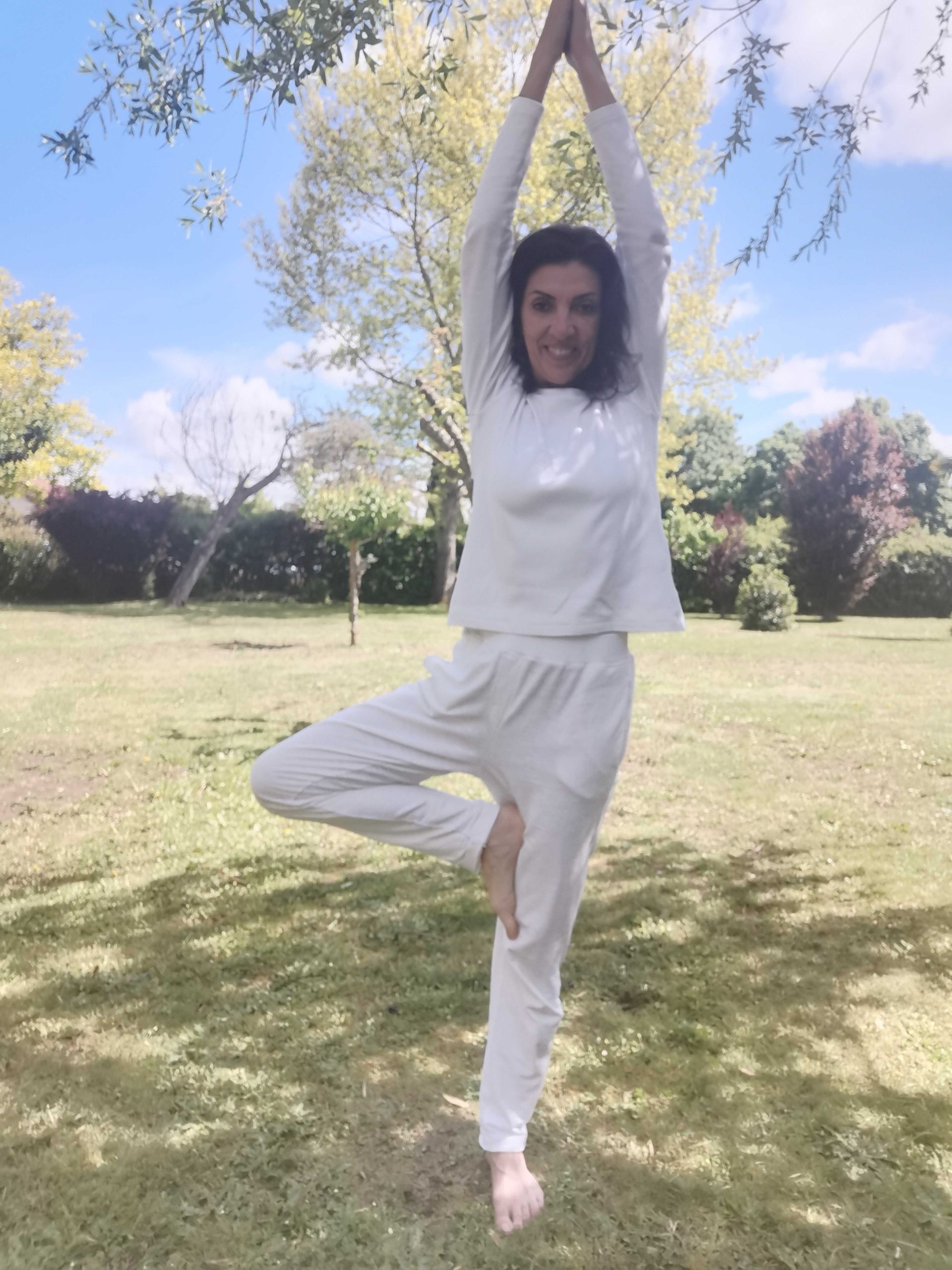 Personne en posture de yoga Vrksasana dans un parc ensoleillé.