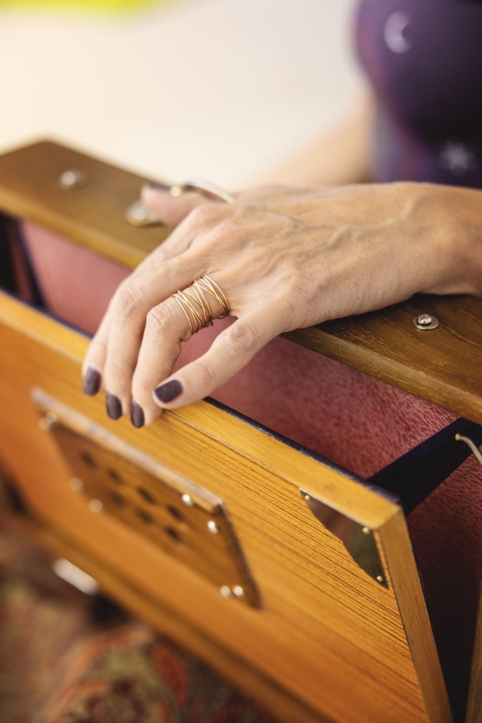 Main ornée de bagues posée sur un harmonium en bois.