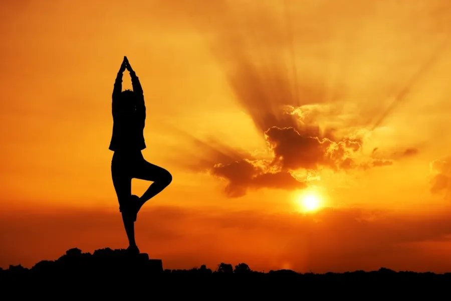 Personne en posture de yoga sur fond de coucher de soleil.