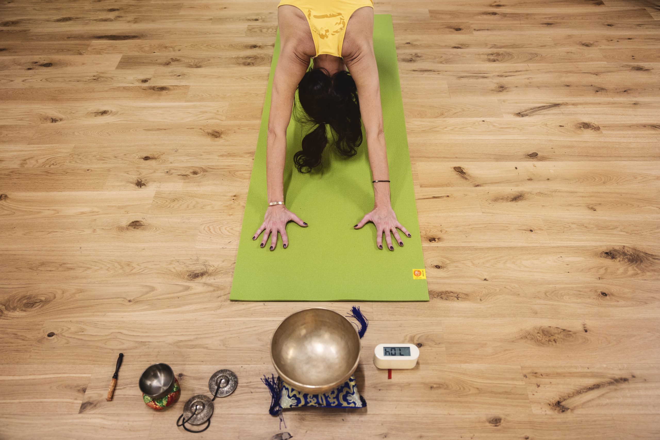 Femme en posture de yoga sur tapis vert avec bols et accessoires.